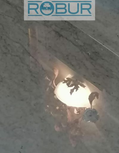 Dettaglio di un pavimento in marmo lucidato a specchio, con riflesso nitido di una lampada decorativa.